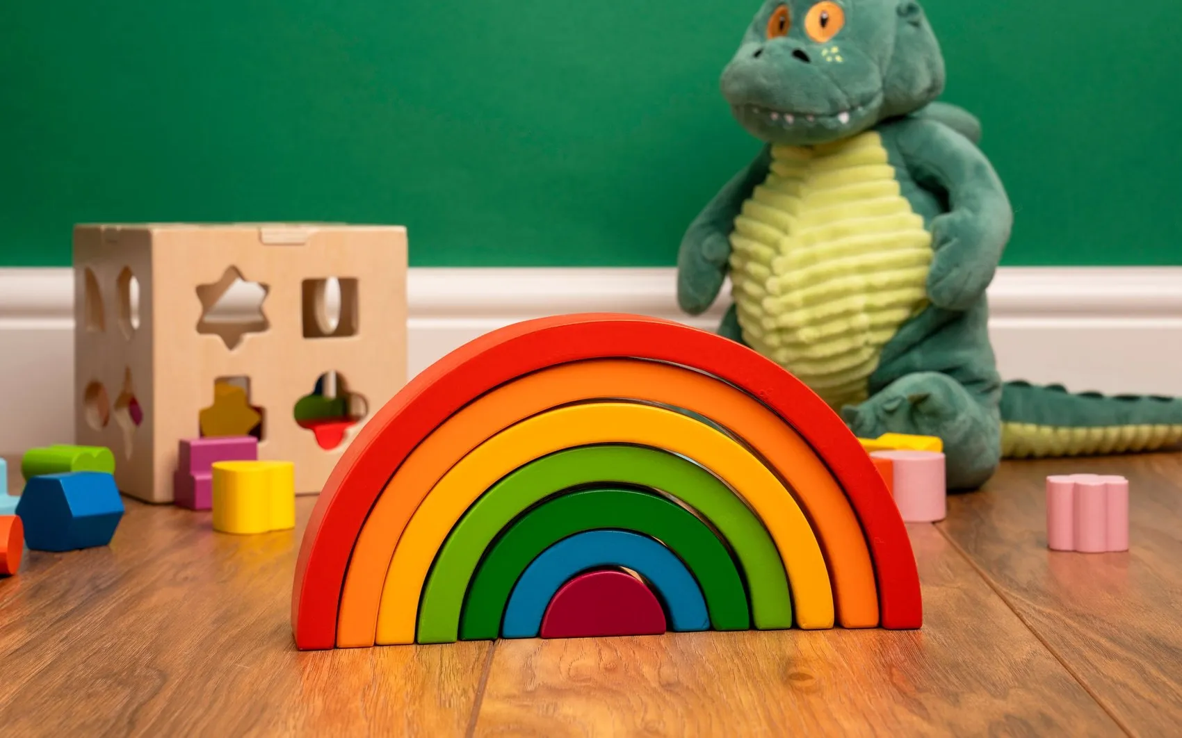 Pelangi kayu susun dan boneka buaya di lantai kamar anak